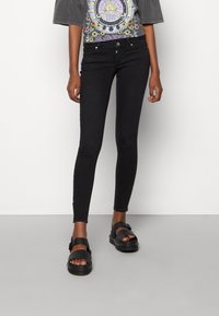 Jeans negros ajustados con una textura suave, que presentan un diseño de cinco bolsillos y un ajuste ceñido. Combinados con sandalias negras gruesas.