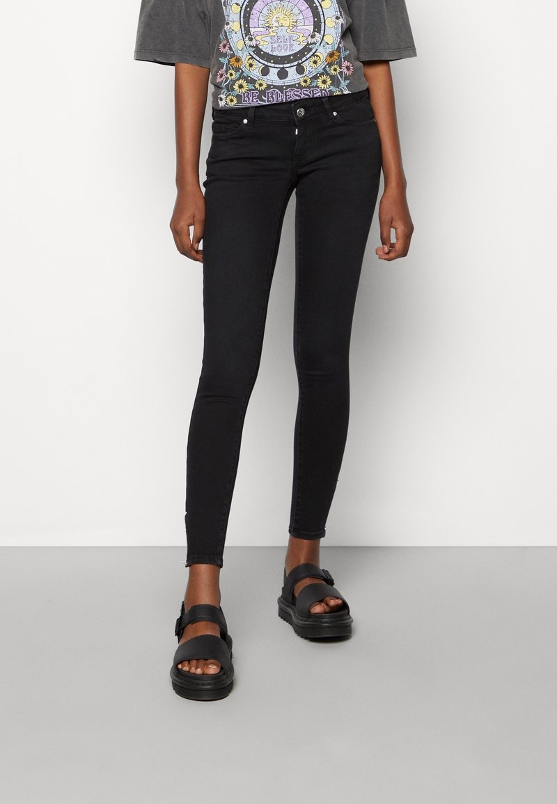 Jeans negros ajustados con una textura suave, que presentan un diseño de cinco bolsillos y un ajuste ceñido. Combinados con sandalias negras gruesas.