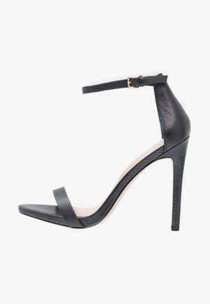 Sandale noire à talons hauts avec une lanière de cheville, en matériau texturé, à bout ouvert et à talon stiletto élancé. Semelle intérieure de couleur neutre.