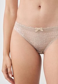 Mutande in pizzo nudo con motivi floreali, bordi ondulati e un piccolo fiocco decorativo sul davanti. Tessuto morbido e design a vita bassa.