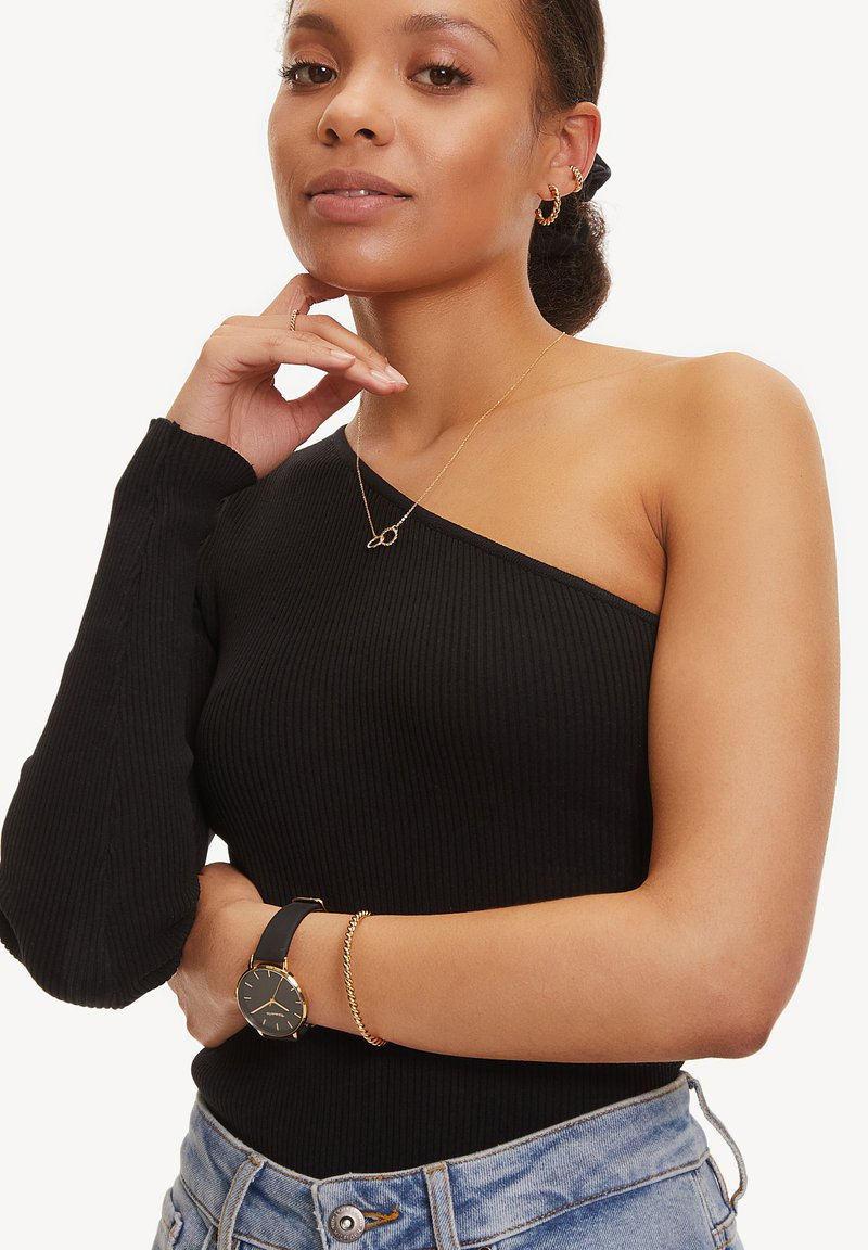 Schwarzer Rippeneinschulter-Bodysuit mit langem Ärmel, kombiniert mit einer goldenen Halskette und einer schwarzen Uhr. Das Modell trägt hellblaue Jeans.