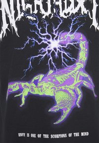Camiseta negra con un gran gráfico de un escorpión en verde y púrpura, con texto blanco debajo. Diseño abstracto de relámpagos en el fondo.