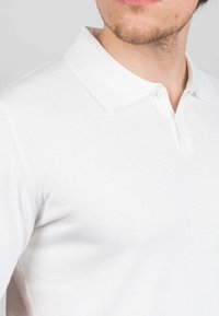 Polo bianco realizzato in cotone morbido. Caratterizzato da un colletto classico, una chiusura a tre bottoni e una silhouette aderente con una sottile trama a coste.