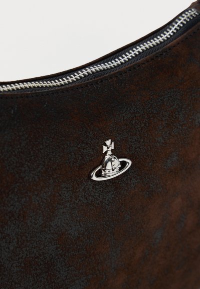 Τμήμα τσάντας από καφέ σκούρο δερματίνη με υφή, με ασημένιο φερμουάρ και μικρό μεταλλικό έμβλημα σε σχήμα πλανήτη με σταυρό στην κορυφή.