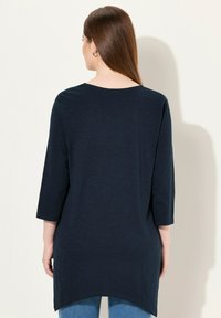 Mörkblå, lång tunika med en avslappnad passform och 3/4-ärmar. Mjuk, strukturerad tyg. Rundad nederkant som sträcker sig något längre bak.