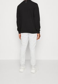 Sudadera negra con cuello redondo, puños y dobladillo de canalé, combinada con pantalones deportivos gris claro con puños elásticos y bolsillos laterales.