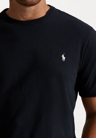 Melns kokvilnas T-krekls ar īsām piedurknēm, ribota apkakle un mazs kontrastējošs izšūts logotips uz krūtīm. Gluda tekstūra.