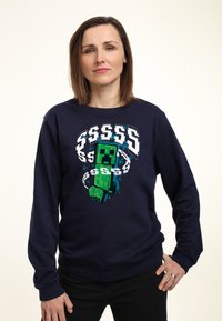 Sudadera azul marino con un gráfico de un personaje pixelado en verde. Mangas largas, cuello redondo, tela suave, con acentos en blanco y azul agua.
