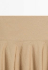 Beige stof med en vandret søm og bløde, uregelmæssige folder under sømmen.