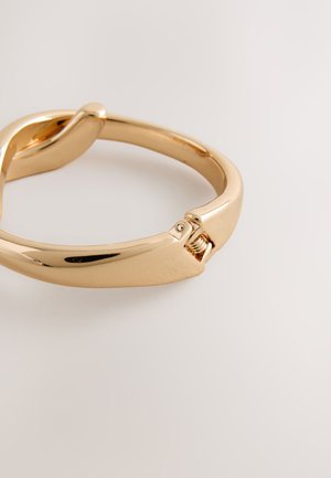 Gold-tone metal bracelet with a smooth, curved design and a clasp featuring a coiled spring detail for secure closure.