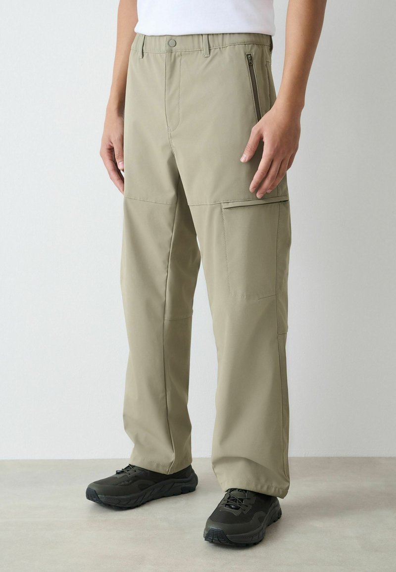 Bēšas kravas bikses ar rāvējslēdzēja kabatām, elastīgu jostasvietu un taisnām kājām. Izgatavotas no viegla, izturīga auduma.