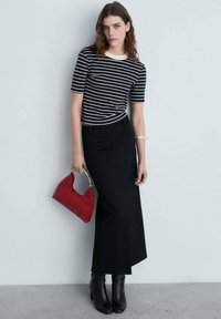 Gestreiftes navy- und weißes Kurzarmoberteil, hoch taillierter Nadelstreifenrock, rote Handtasche, schwarze Stiefeletten mit Absatz vor einem hellen Hintergrund.