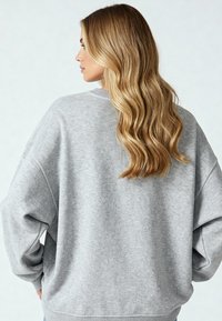 Vaaleanharmaa ylipitkä collegepaita, jossa on ribattu hihansuut ja helma. Pehmeä tekstuuri, rento istuvuus ja epämuodollinen muotoilu. Näkyvät takakainalon yksityiskohdat.