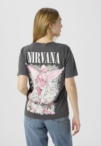 Grå bomulls-t-skjorte med en stor, detaljert rosa og hvit grafikk av en figur med vinger og blomster på baksiden. Forsiden har teksten "NIRVANA".
