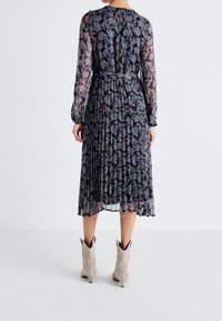 Mönstrad midiklänning med långa genomskinliga ärmar, plisserad kjol och figursydd midja. Bakpartiet har en stängning i halsen, i kombination med ljusgrå stövlar.