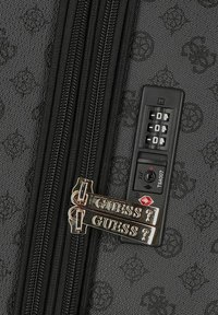 Valigia in tessuto nero con chiusura lampo testurizzata e due etichette dorate embossate con la scritta "GUESS". Dispone di un meccanismo di chiusura a combinazione approvato dalla TSA.