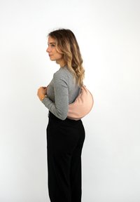 Ljust rosa axelväska i mjukt material, semikurvad form, med dragkedjestängning, bärs på ryggen, kombineras med grå långärmad topp.