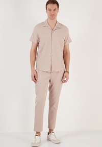 Camisa corta de manga corta de color marrón claro con rayas verticales, pantalones de color marrón claro a juego y zapatillas blancas. Tejido suave con una textura sutil.