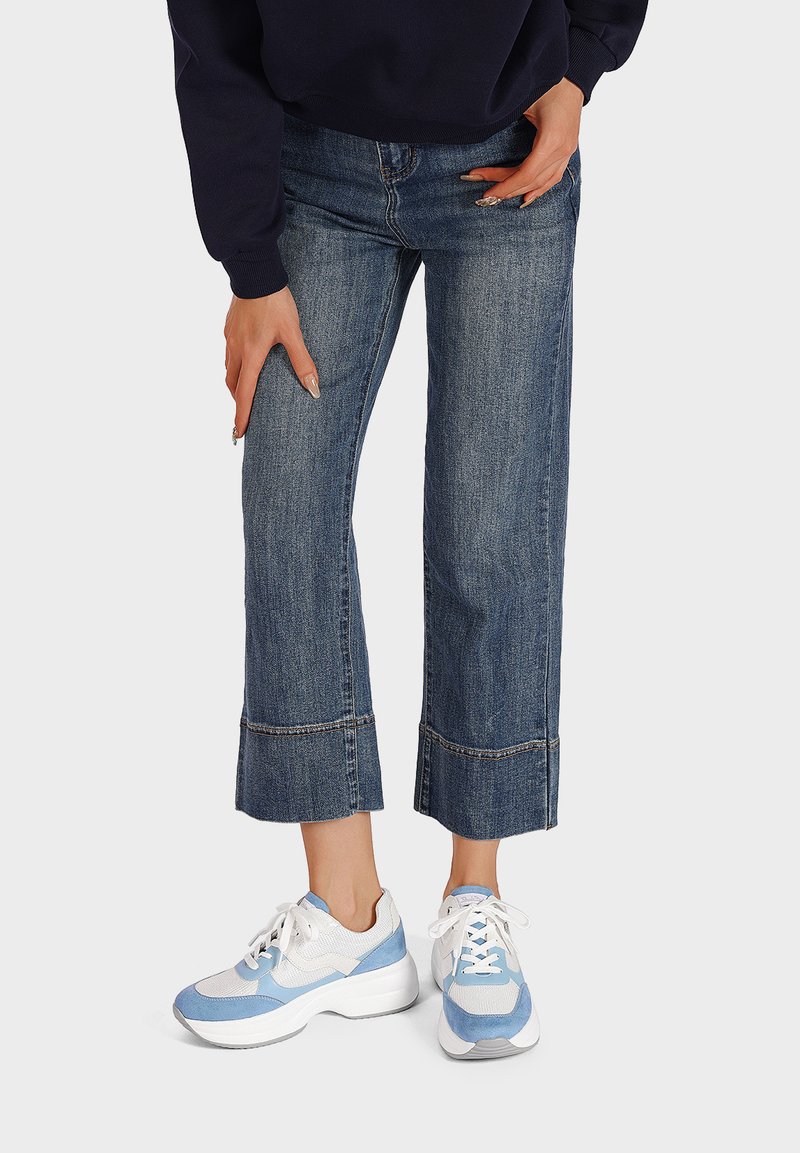 Jeans cropped in denim con un lavaggio blu chiaro e orlo sfrangiato, abbinati a sneakers blu e bianche con suola spessa e dettagli in mesh.