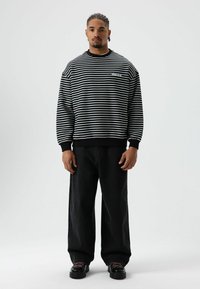Sweat-shirt à rayures noires et blanches avec un col rond, associé à un jean noir ample et des chaussures noires avec des accents rouges. Look décontracté simple.
