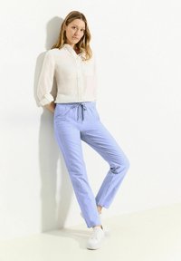Světle modré lněné kalhoty s elastickým pasem a šňůrkou, doplněné bílou košilí s knoflíky. Bílé tenisky outfit dokončují.