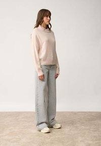 Jasnoróżowy sweter o luźnym kroju i wywiniętym kołnierzem, zestawiony z jasnoszarymi dżinsami o wysokim stanie i szerokimi nogawkami oraz jasnymi trampkami.