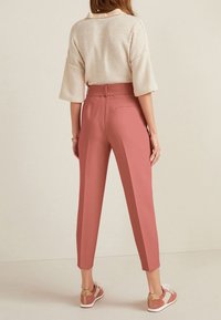 Pantalons tailleur roses à taille haute, avec poches arrière et jambes fuselées, associés à un pull texturé crème et des chaussures de sport.