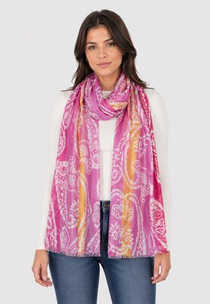 Woman wearing a bright pink, orange, and white paisley patterned scarf over a white long-sleeve top and blue jeans.