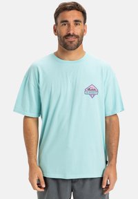 Light blue cotton T-shirt with a box logo featuring a pink eye emblem. Oversized fit, short sleeves, and a crew neck design.