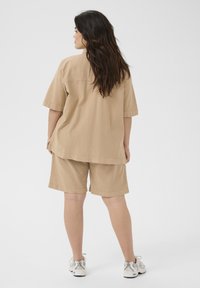 Chemise en coton beige oversize à manches courtes assortie à un short. Le tissu a une texture lisse. Des baskets blanches complètent la tenue.