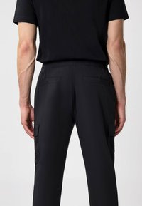 Zwarte cargobroek met elastische tailleband, voorzien van twee achterzakken en mesh-details aan de zijkant voor extra ventilatie.