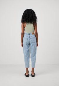 Hellgrünes, geripptes Tanktop und hellblaue, hochtaillierte Jeans. Die Jeans haben eine lässige Passform, umgekrempelte Säume und ein braunes Markenetikett auf der Rückseite.