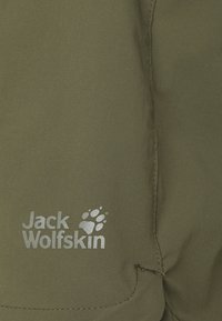 Oliivivihreät kangashousut, joissa on sileä pinta, ommellut saumat ja hopeinen "Jack Wolfskin" -logo, jossa on tassunjälkimuotoilu.