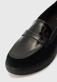 Mocassins noirs avec un dessus en cuir verni brillant et un bas en daim texturé, dotés d'une semelle plate et fine et de détails cousus.