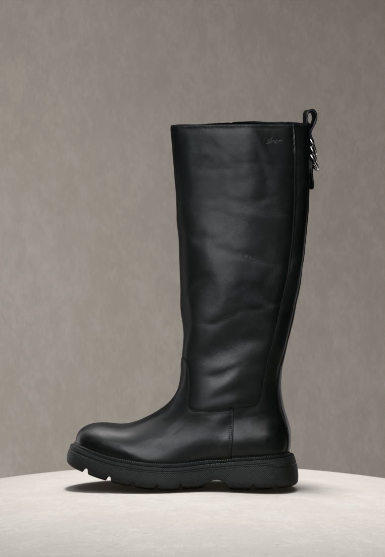 Botte haute en cuir noir avec bout arrondi, semelle épaisse à relief et languette avec anneau métallique à l'arrière.