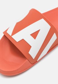 Coral slip-on sandal with a textured footbed and wide strap featuring raised white letters 'A' and 'V.' Smooth, matte finish.