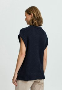 Marineblauer Strickpullover mit kurzen Ärmeln, geripptem Ausschnitt und Saum sowie strukturiertem Stoff. Von hinten gezeigt, kombiniert mit hellen Hosen.