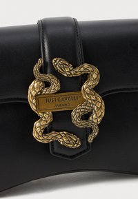 Zwarte leren handtas met een gestructureerd oppervlak, voorzien van een gouden slangenvormige sluiting en een metallic logoplaat met de tekst "JUST CAVALLI MILANO."