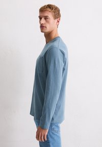 Koszula z długim rękawem w jasnoniebieskim kolorze, wykonana z miękkiego materiału, z kieszonką na piersi i okrągłym dekoltem, zestawiona z jasnoniebieskimi dżinsami.