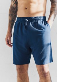 Pantalones cortos deportivos de color azul marino con cinturilla elástica, cordón y tejido suave. Terminan justo por encima de la rodilla sin logotipos ni diseños visibles.