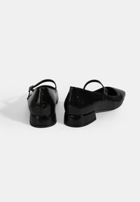 Ballerines en cuir verni noir avec un bout pointu et une bride à l'arrière, dotées d'un petit talon bloc et d'un design texturé.
