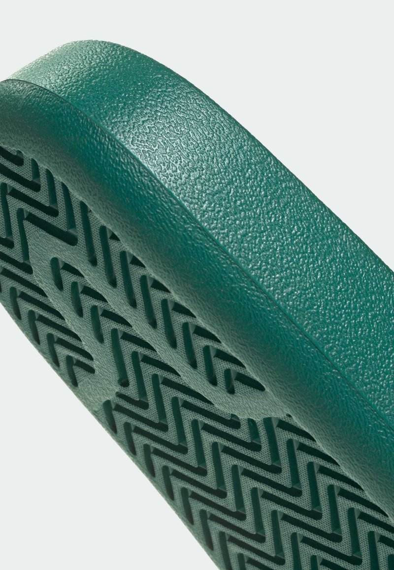 Grønt tekstureret materiale med en mønstret sål med zigzag-riller; kanten er afrundet og glat for ergonomisk pasform.