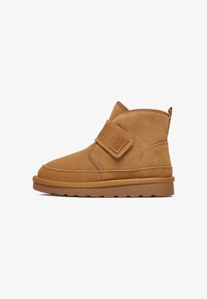 Stivaletti alla caviglia in camoscio color tan con cinturino a strappo, punta arrotondata e sottili dettagli di cucitura sulla suola e sulla tomaia. Suola piatta in gomma.