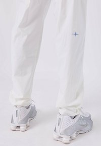 Pantalons de sport blancs avec un logo étoile bleu subtil sur la jambe gauche, associés à des chaussures de course Nike grises et blanches présentant un design de talon distinctif.