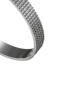 Silver bracelet with a textured, pyramid-stud design on one side and a smooth metallic finish on the other. Sleek, curved shape.