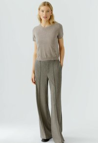 Beige kurzärmliger Pullover mit einem dekorativen, mit Perlen besetzten Ausschnitt, kombiniert mit hoch taillierten, weit geschnittenen karierten Hosen in Grau und Schwarz.
