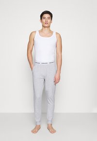 Witte tanktop en grijze katoenen sweatpants met elastische tailleband en boorden. De broek heeft een zwart logo op de tailleband.