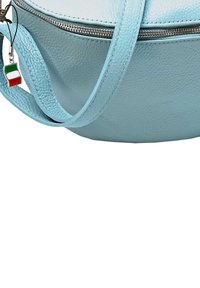 Helles blaues Lederhandtasche mit einer strukturierten Oberfläche, ausgestattet mit einem Reißverschluss und einem dekorativen Charm in Form einer italienischen Flagge.