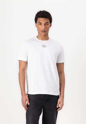 White cotton t-shirt with short sleeves, round neck, and a small gray logo on the chest. Paired with dark denim jeans.