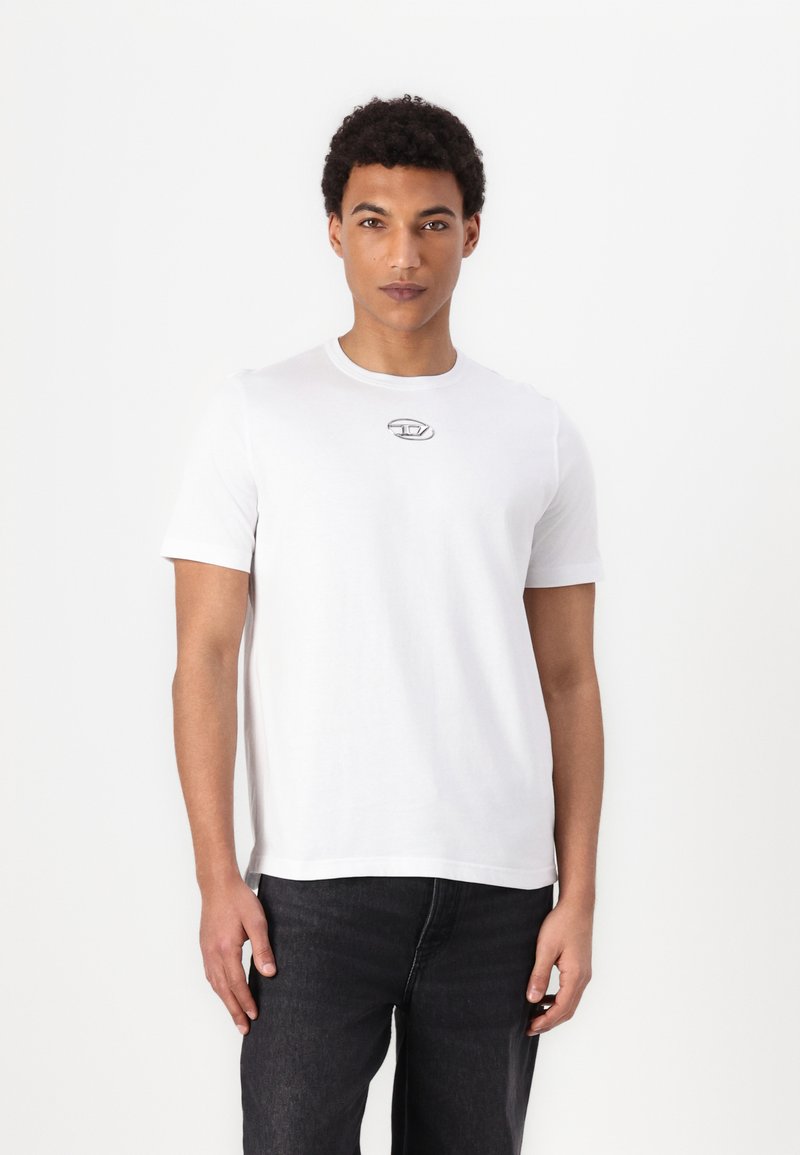 Hvid bomulds T-shirt med korte ærmer, rund hals og et lille gråt logo på brystet. Sammen med mørke denim jeans.